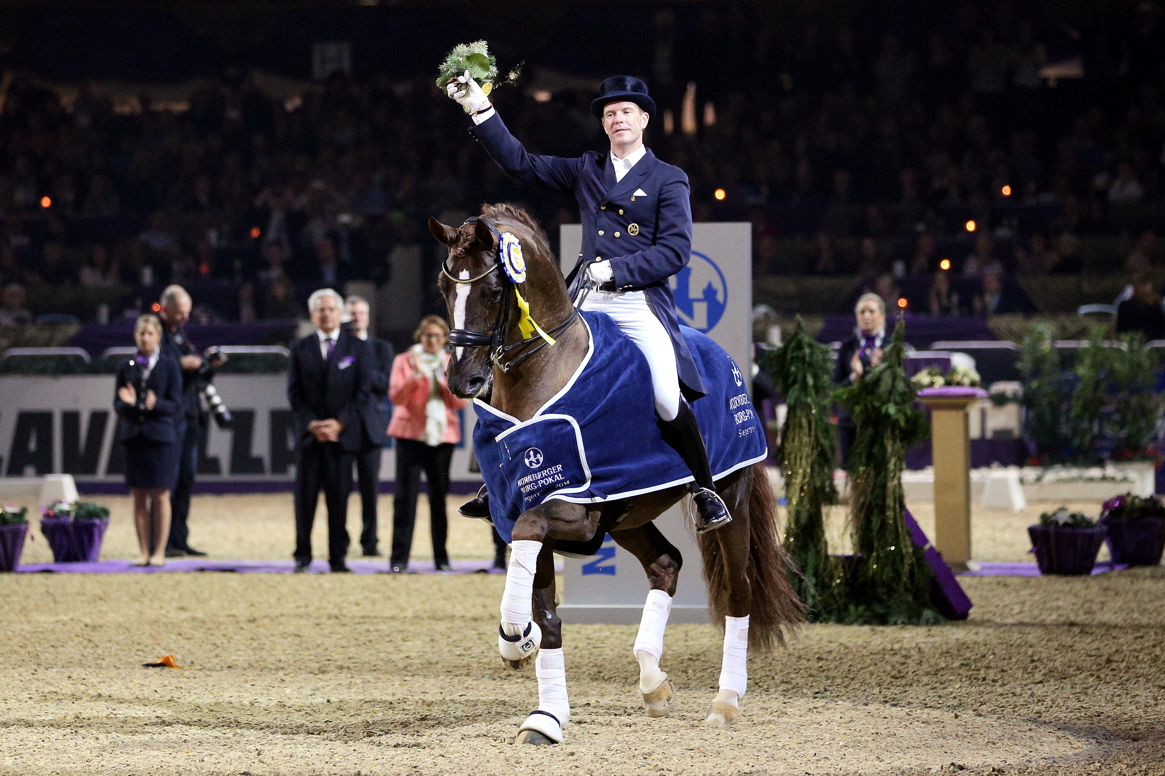 Hengst mit Decke und Reiter mit Blumen in der Hand lassen sich feiern